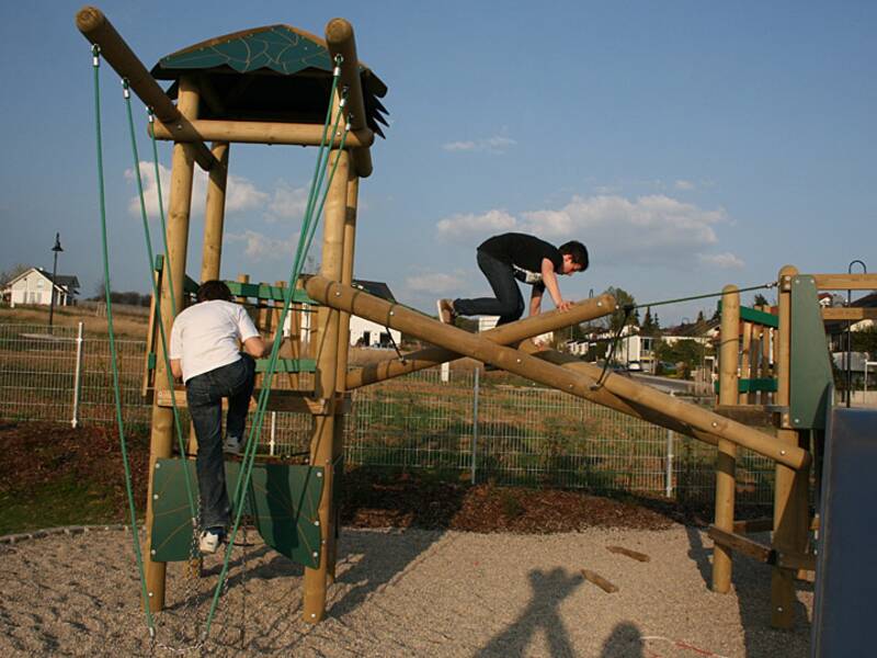 Zwei Personen klettern auf einem Spielplatzgerüst aus Holz.